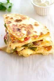 Stack of cheesy vegetable quesadillas cut into triangles and served on a white surface.