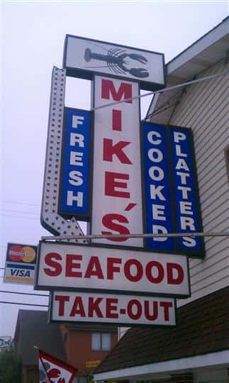 a closeup of the mike's seafood sign that also says takeout, fresh, cooked and platters on it