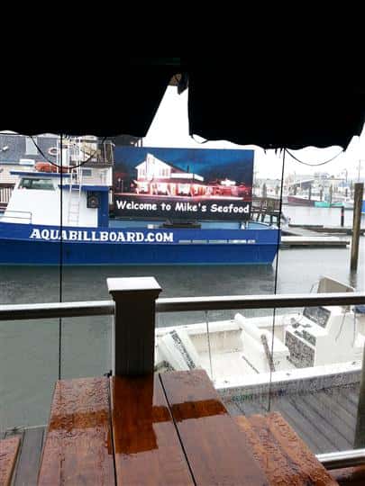 a billboard on a boat that says "welcome to mike's seafood" with a photo of the storefront