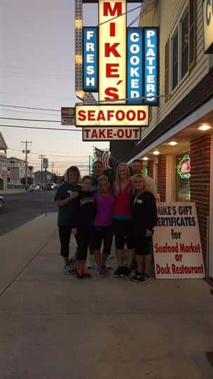 a group of 9 people posing under the mike's seafood sign
