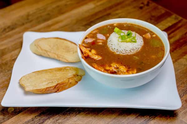 Bowl of gumbo soup topped with rice, served with slices of bread