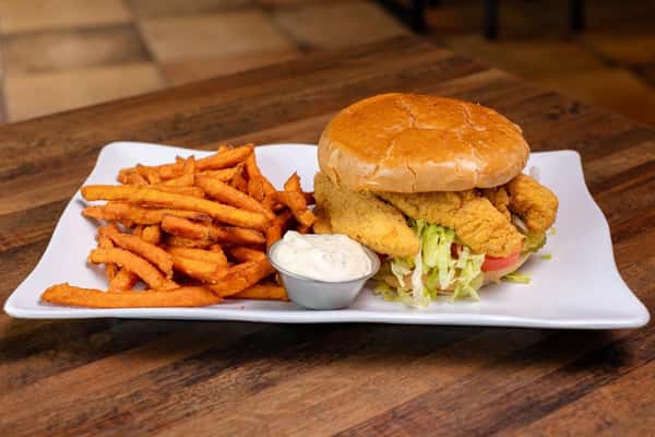 Fried shrimp po'boy sandwich with sweet potato fries and a dipping sauce, on a wooden table