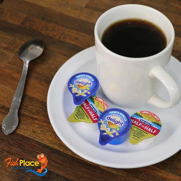Cup of coffee on a saucer with a spoon and Fish Place branded mints, on a wooden table
