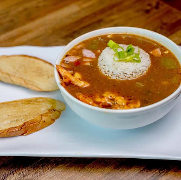 Bowl of gumbo soup topped with rice, served with garlic bread