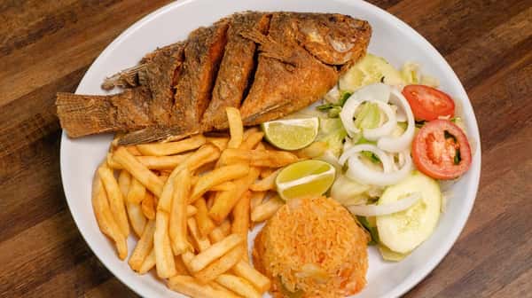 Whole fried fish served with french fries, onions, lime, and a side