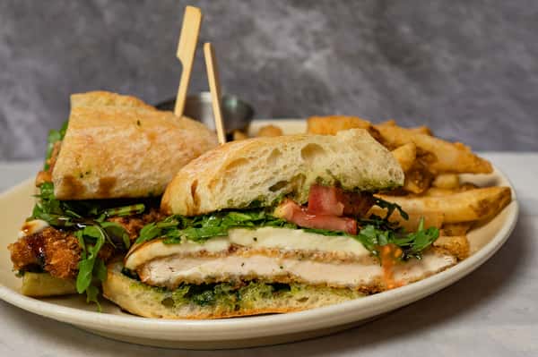 Crispy chicken sandwich with arugula, tomato, mozzarella, and pesto on ciabatta bread, served with golden French fries.