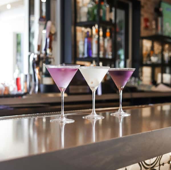 Three martini glasses with colorful cocktails—two purple and one white—elegantly displayed on a sleek bar counter.