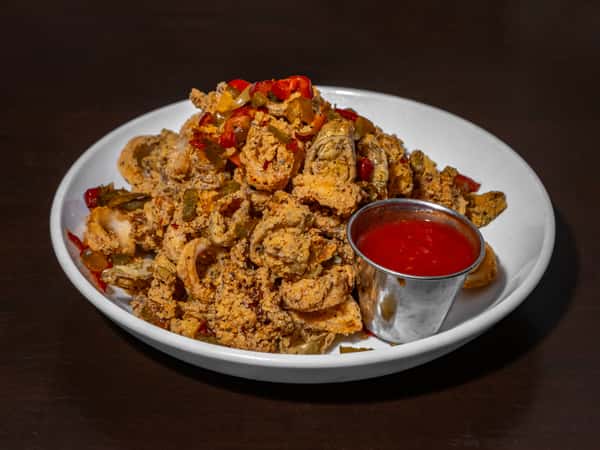 Crispy fried calamari topped with sautéed peppers, served with a side of marinara sauce in a white bowl.