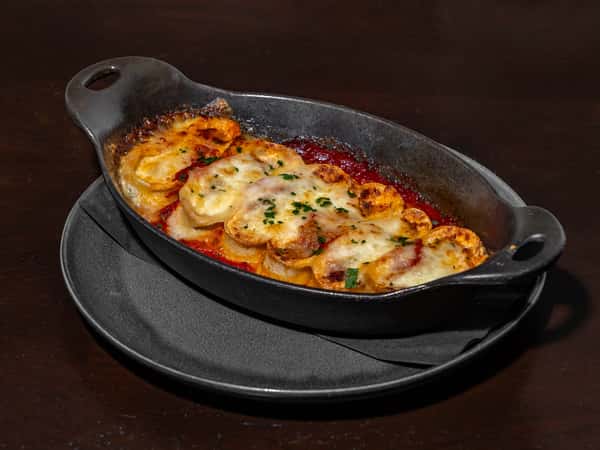 Baked cheese-covered eggplant rounds in marinara sauce, served in a cast iron dish with a sprinkle of parsley.