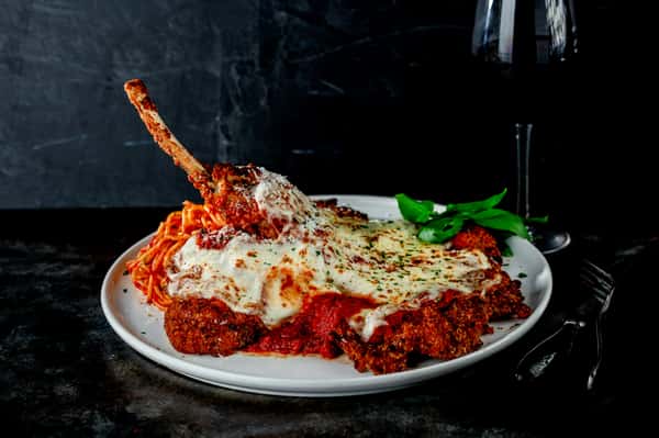 Tomahawk pork chop parmesan topped with melted mozzarella and marinara, served with spaghetti and fresh basil.