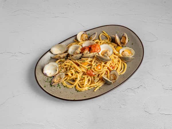 Linguine with clams in open shells, cherry tomatoes, and fresh herbs served on a rustic oval plate.and crispy topping in a white bowl.