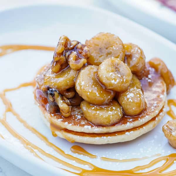 Fluffy pancakes topped with caramelized bananas, walnuts, powdered sugar, and drizzled with caramel sauce.