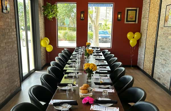 Elegant private dining room setup with a long table, yellow balloons, flower centerpieces, and place settings for a celebration.