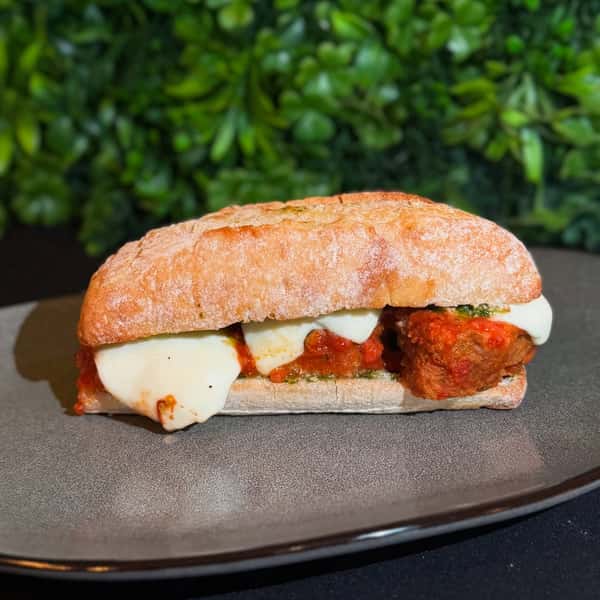 Meatball sub on ciabatta bread with marinara sauce, melted mozzarella, and pesto.