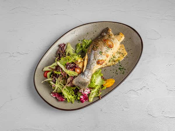 Whole roasted fish served over a bed of mixed greens with cherry tomatoes and a slice of grilled polenta.