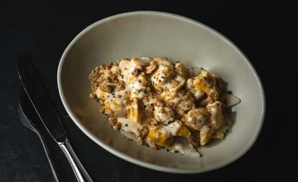 Butternut squash ravioli topped with a creamy sauce, toasted nuts, and fresh herbs in a shallow white bowl.