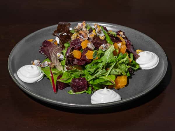 Mixed greens salad with golden and red beets, candied nuts, and whipped goat cheese dollops on a dark plate.