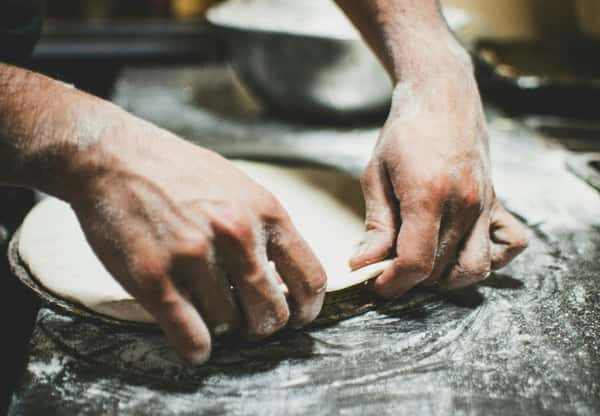 Chef shaping fresh pizza dough on a floured surface, preparing for a handmade crust in a rustic kitchen setting.
