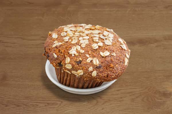 Raisin bran oat muffin topped with rolled oats on a white plate.