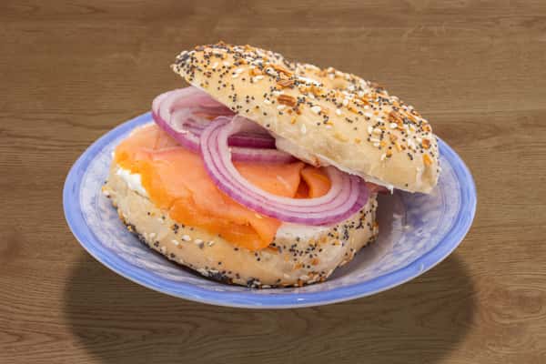 Close-up of a smoked salmon and cream cheese bagel with sliced red onion.