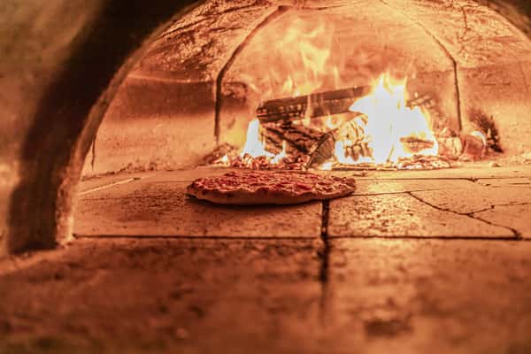 A close-up of a pizza baking in a wood-fired oven.