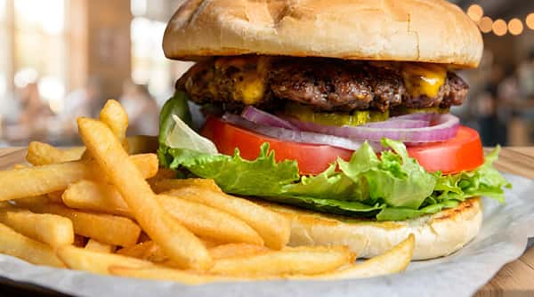 Cheeseburger with lettuce, tomato, onion, pickles, and a side of french fries.