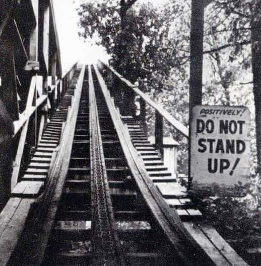 Vintage photo of an old wooden roller coaster with sign saying "DO NOT STAND UP!"