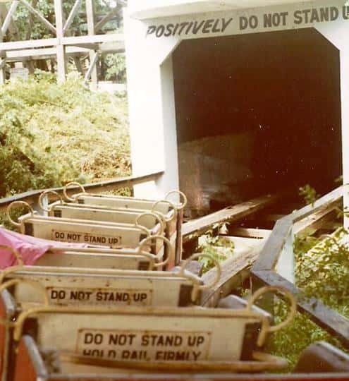 Photo of roller coaster going into a dark tunnel withs signs that read "Do NOT STAND UP HOLD RAIL FIRMLY"