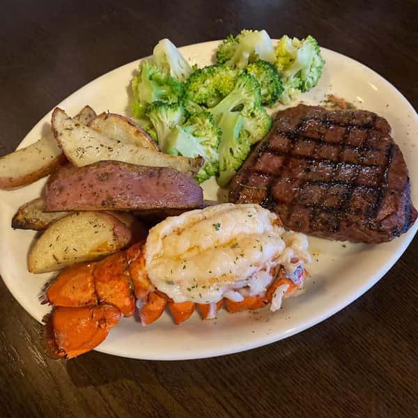 Steak and lobster dinner with a side of wedged potatoes and cooked broccoli