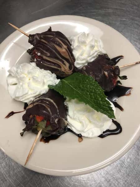 Chocolate dipped strawberries topped with whipped cream and a mint leaf garnish