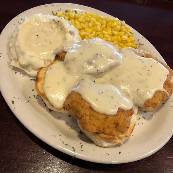Biscuits covered in gravy with a side of mashed potatoes and corn