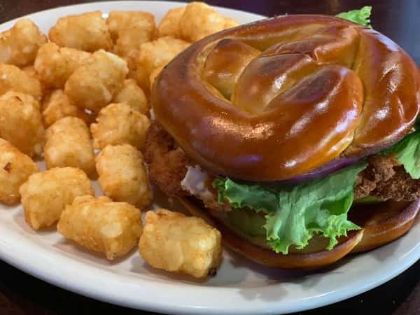 Fried chicken sandwich with a pretzel bun and a side of tater tots