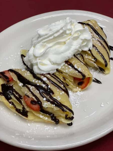 Crepes with chocolate drizzle, powdered sugar, strawberries, and whipped cream on top