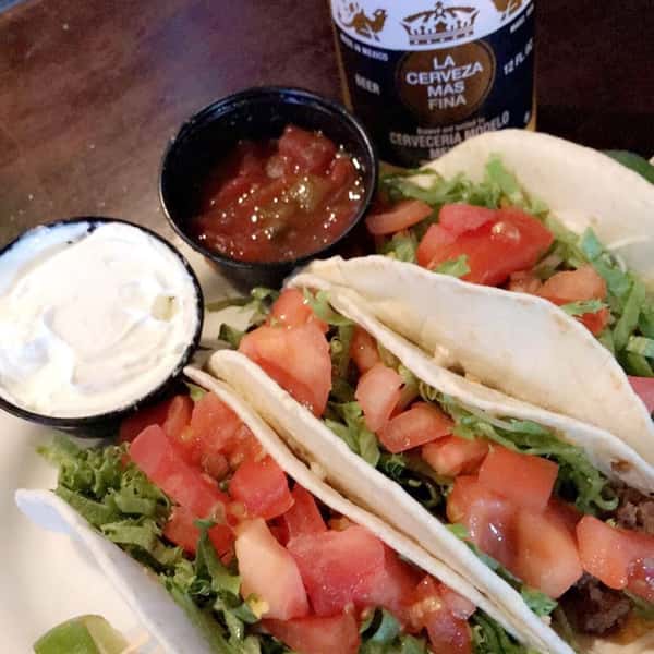 Tacos topped with tomatoes and lettuce, with a side of salsa and sour cream