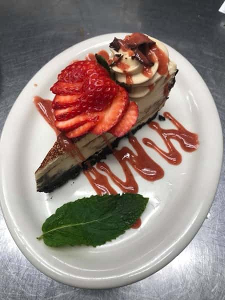A sliver of cake topped with strawberry syrup, fresh strawberries, and a mint leaf garnish