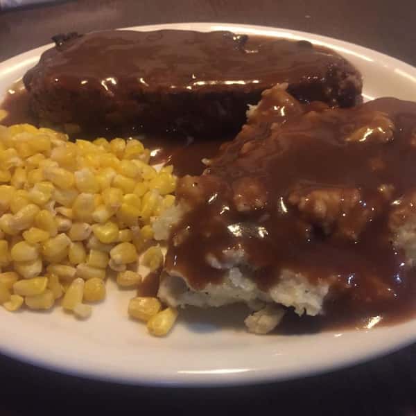 Beef topped with gravy and a side of mashed potatoes, and corn