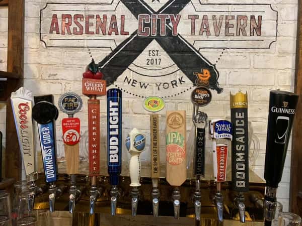 Beer taps in front of a Brick wall with Arsenal city Tavern painted on it.