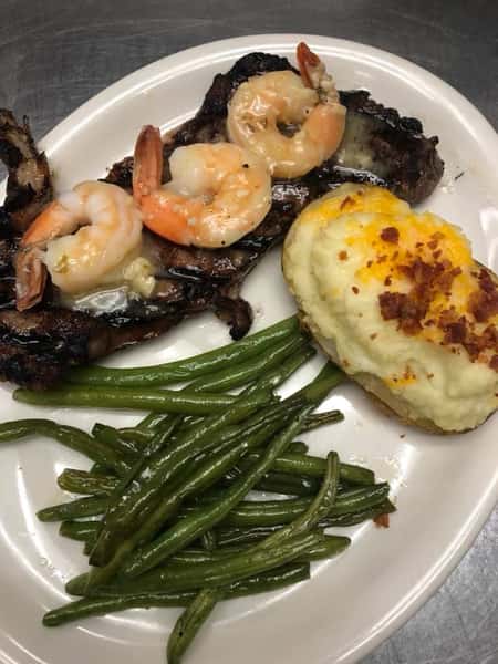 Steak topped with grilled and buttered shrimp with a side of mashed potatoes and green beans