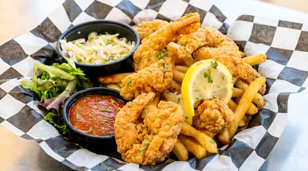 Fried shrimp and french fries with a lemon wedge, coleslaw, side salad, and cocktail sauce in a checkered paper-lined basket.