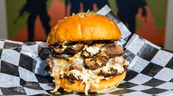 A large burger with melted cheese and mushrooms on a bun, served on checkered paper with a soldier mural background.