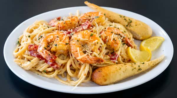 Shrimp pasta with creamy sauce, sun-dried tomatoes, parmesan, parsley, garlic breadsticks, and lemon wedges.