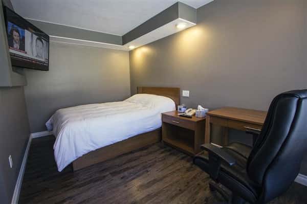 Room with single bed, nightstand, desk, rolling chair, television set in wall.