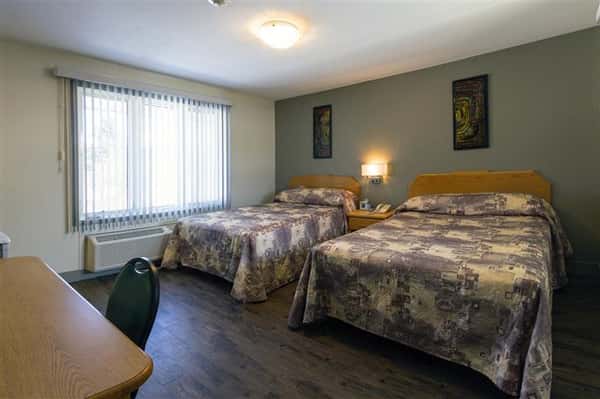 Room with two beds, nightstand, in-wall air conditioner, desk with chair