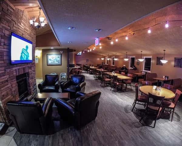 Lounge room with fireplace, television, leather chairs adjacent to dining tables and booths.