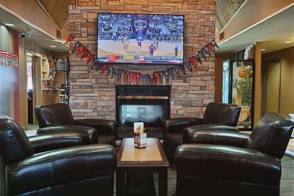 Lounge room with TV set on wall above fireplace, coffee table and four leather chairs