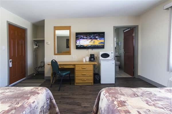 Room with two beds, desk, chair, television on wall, mini fridge and microwave. Bathroom on right, closet on left.