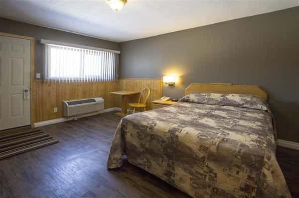 Room with wood floors, bed, small wooden table and chair, night stand, in-wall air conditioner.