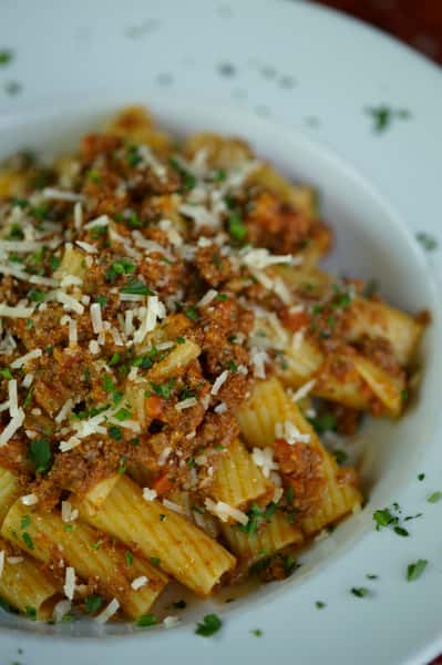 Rigatoni pasta topped with rich Bolognese sauce, grated Parmesan, and fresh parsley served in a white bowl.