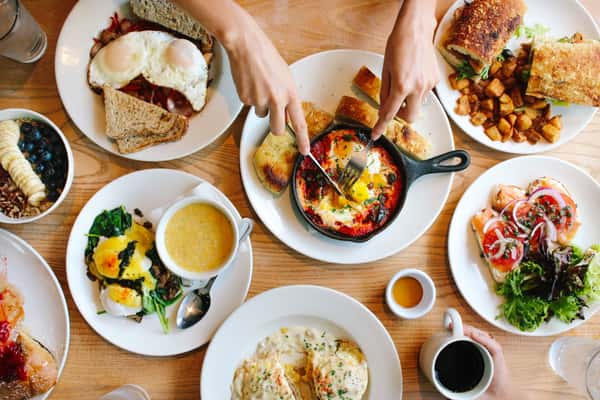 Colorful brunch spread with shakshuka, eggs Benedict, biscuits and gravy, fresh fruit, sandwiches, and coffee on a wooden table.