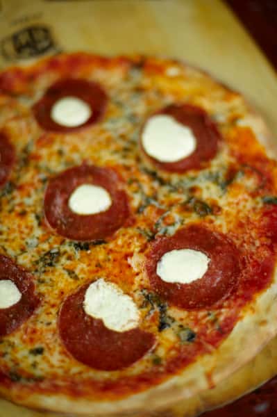 Freshly baked pepperoni pizza topped with melted cheese, tomato sauce, and dollops of creamy ricotta on a wooden board.